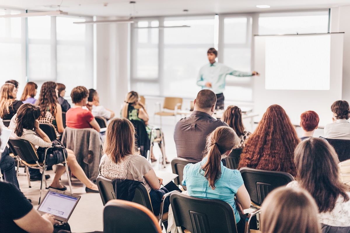 Business and entrepreneurship symposium. Speaker giving a talk at business meeting. Audience in conference hall. Rear view of unrecognized participant in audience. | Virtual Assistant For Doctors