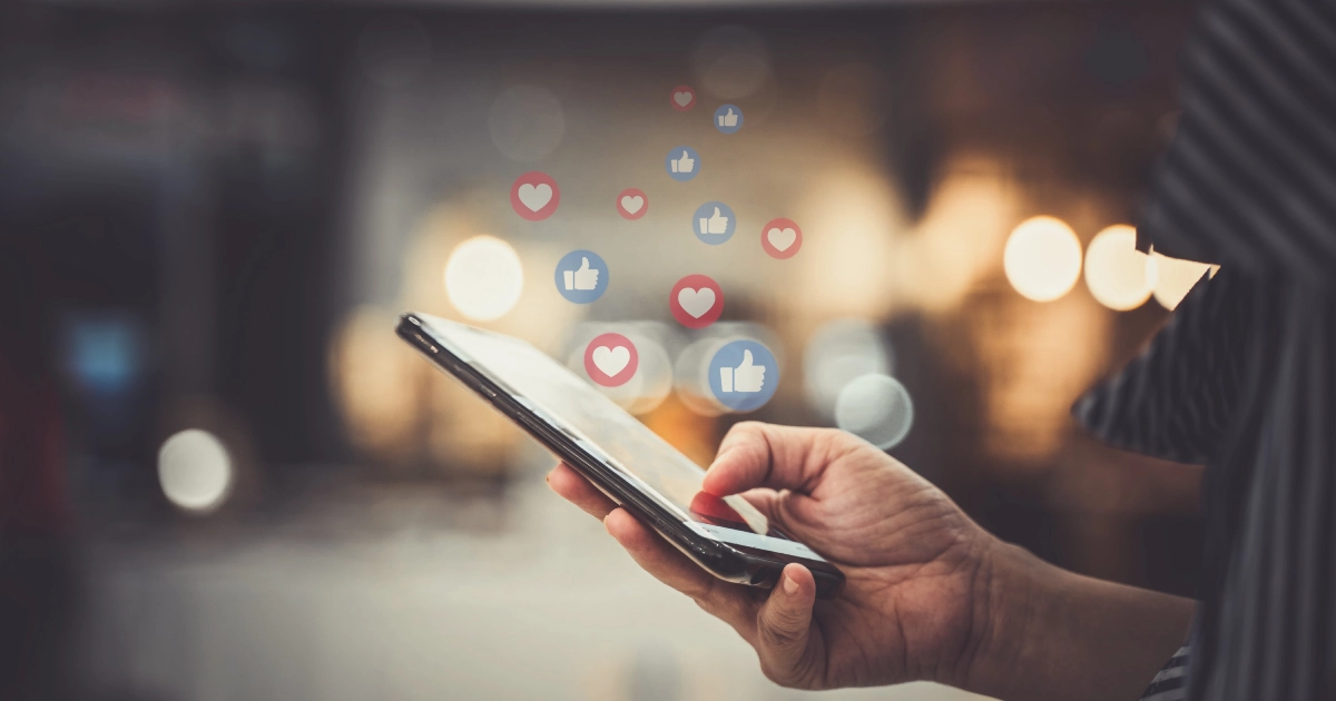 Social Media Assistant using smartphone with floating social media like and heart icons, symbolizing online engagement and digital interaction.
